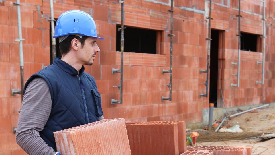 Mann mit Helm trägt Steine auf einer Baustelle