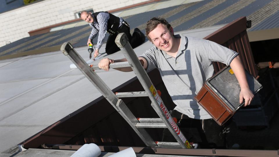 Schüler (vorne auf Leiter) und Handwerksmeister bei Dacharbeiten