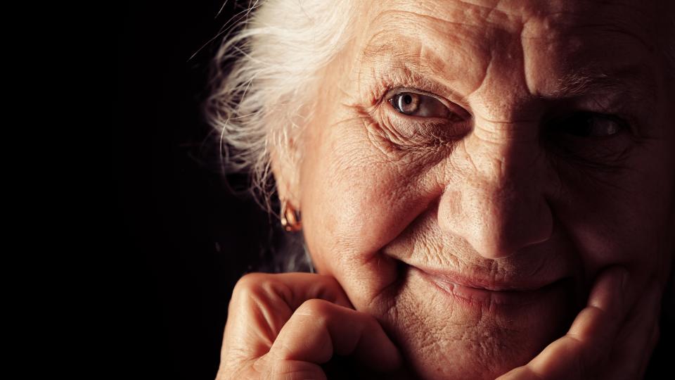 Gesicht einer freundlichen, älteren Dame, die ihrem Kopf auf eine Hand abstützt. 