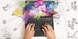 Foto: Multitasking. Businessfrau arbeitet mit Laptop, daneben Zeichnungen Jobaufgaben
