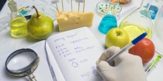 Der Lebensmittelkontrolleur testet Obst vom Markt. Notizbuch mit Forschungsbericht und blauem Stift auf dem Labortisch