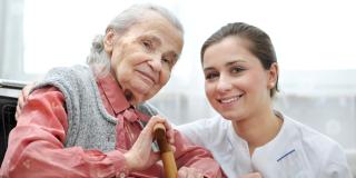 Eine Pflegerin kniet neben einer sitzenden Seniorin